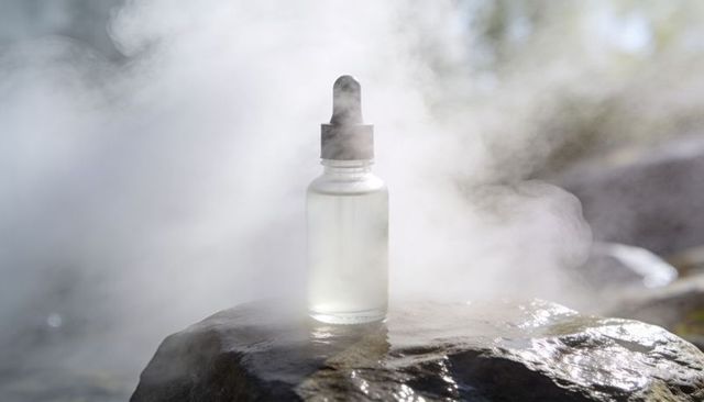 Frosted glass dropper bottle on wet stone with rising mist backlit wellness serum