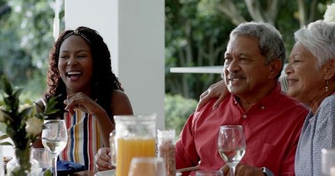 Multigenerational Family Laughing on Sunlit Patio During Casual Brunch with Juice