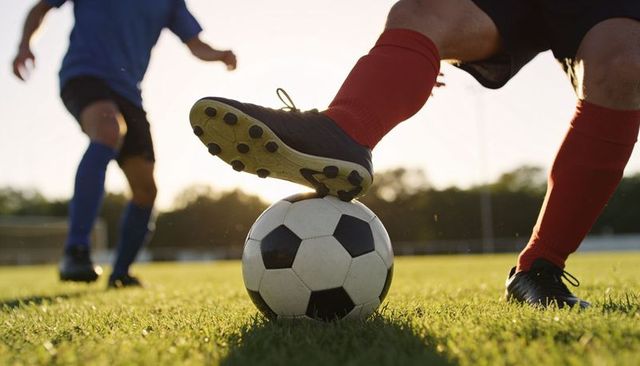 Backlit soccer player controlling ball with cleat on grass during golden hour match
