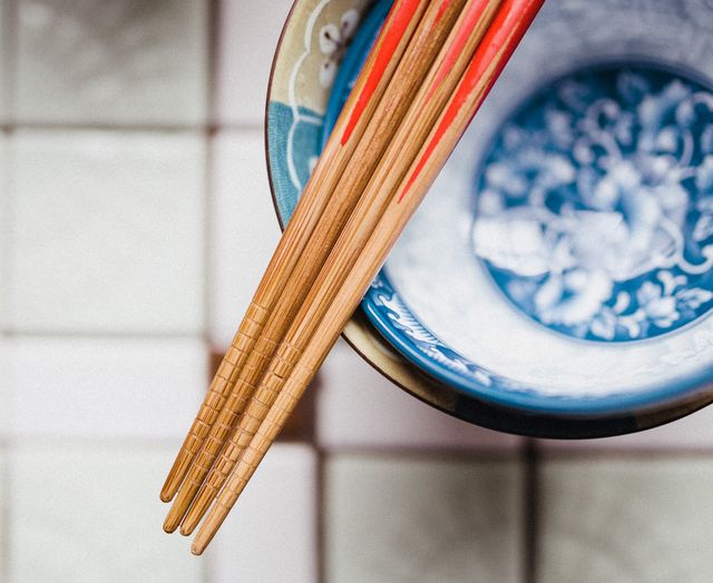 Shows detailed view of wooden chopsticks with red accents resting on a blue and white ceramic bowl. Useful for topics related to Asian culture, dining, utensils, or culinary arts. Suitable for advertising traditional restaurants, food blogs, cooking classes, or cultural education resources.