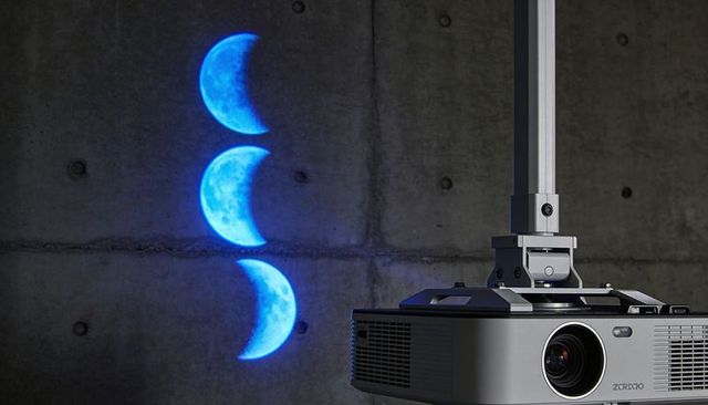 Ceiling-mounted projector casting triple blue crescent moons on industrial concrete wall