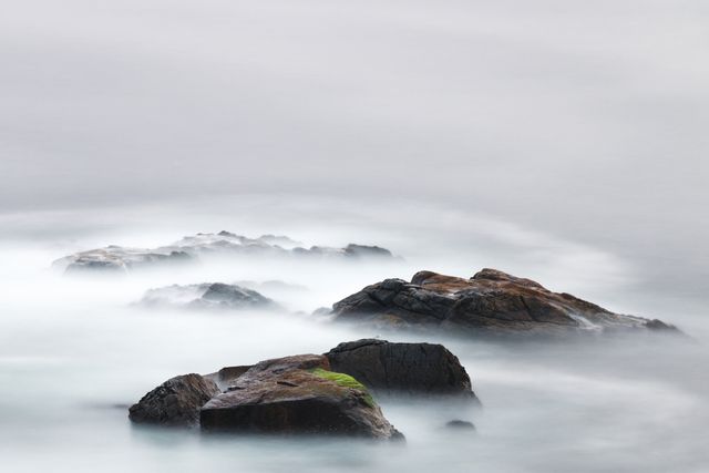 The misty sea over the rocks in a tranquil ocean scene creates a serene and reflective atmosphere. Ideal for use in environmental campaigns, travel brochures, meditation themes, artistic prints, or as a calming background in digital projects.
