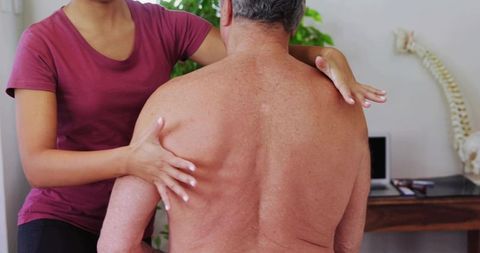 Physical therapist assessing senior man's back with spinal model for manual therapy