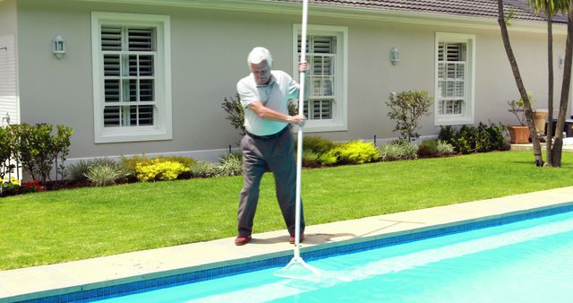 Senior man cleaning swimming pool with net on a sunny day