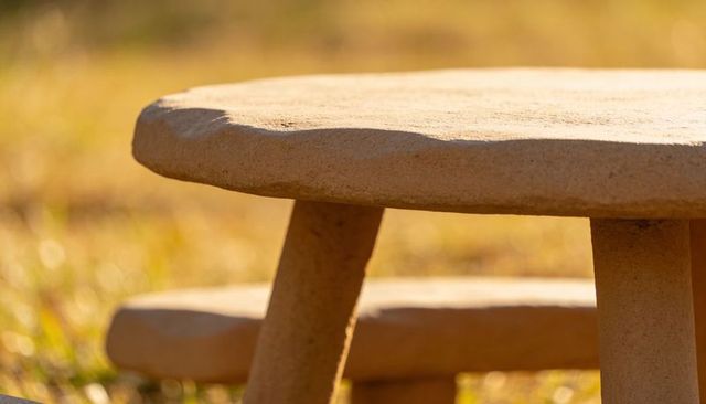 Sunlit stone garden table and bench closeup showing textured concrete top and rounded legs