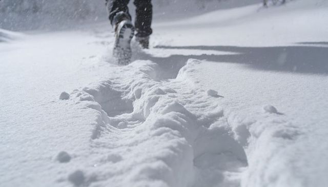 Walking through powder snow leaving deep footprints on winter trail