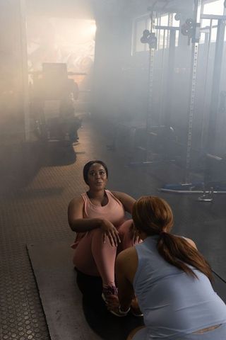 Diverse women performing partner sit-ups in foggy gym with dramatic lighting