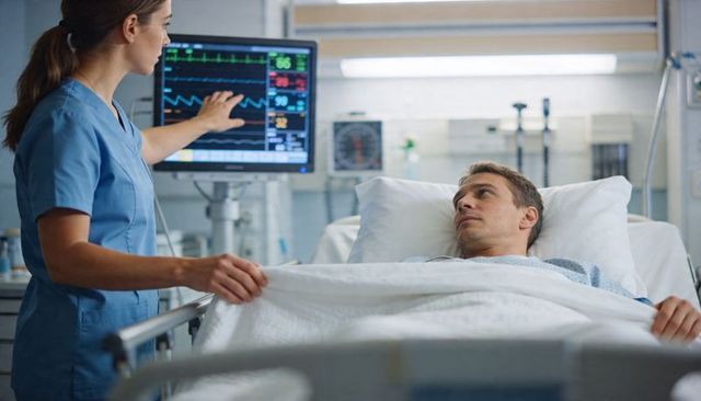 Nurse monitoring cardiac vitals while male patient lying in hospital bed using ecg monitor