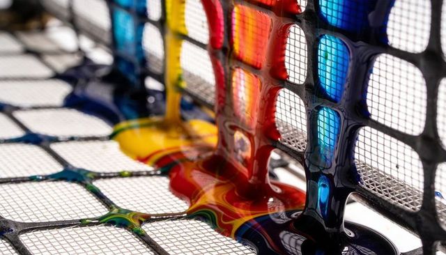 Pouring viscous primary paint through black mesh grid colorful swirls glossy acrylic macro