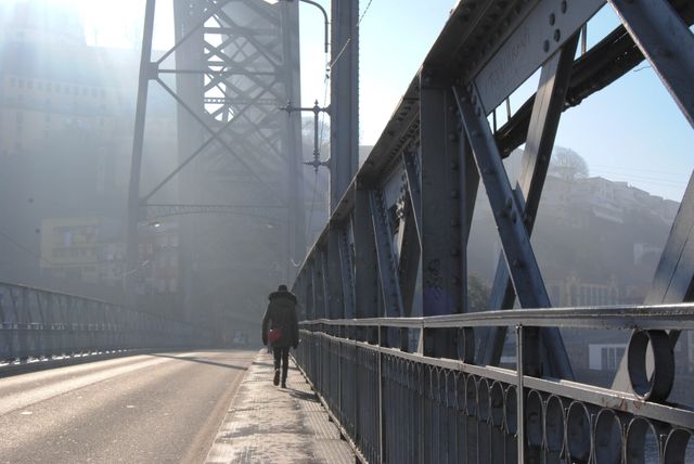 A person walking alone on a misty bridge during a winter morning. The bridge's steel structure is clearly visible, with fog adding a mysterious atmosphere to the urban scene. Ideal for themes like solitude, travel, urban exploration, and atmospheric cityscapes.