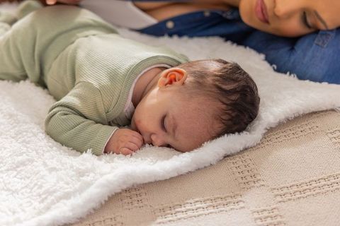 Sleeping infant on plush white blanket with caregiver watching close bonding moment