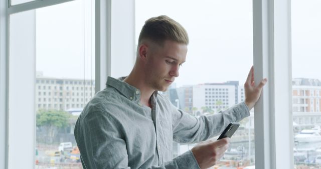 Young Professional Texting on Smartphone by Office Window - Download Free Stock Images Pikwizard.com