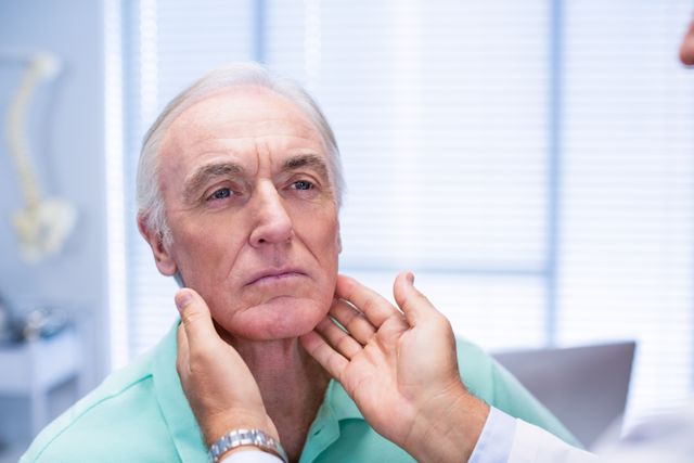 Senior man getting his neck examined by a doctor in a clinical setting. This image can be used for healthcare, medical, or elder care advertisements. Useful for illustrating doctor-patient interactions, clinical exams, and medical diagnostics.