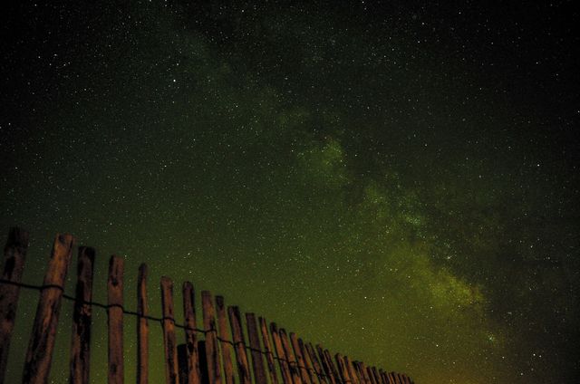 Wooden fence under starry night sky with Milky Way. Suitable for themes of tranquility, nature, and astronomy. Perfect for backgrounds, outdoor lifestyle promotions, or illustrating night scenes.