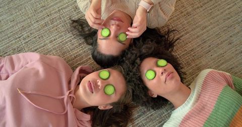 Multicultural women enjoying at-home spa day with cucumber eye slices, cozy self-care trio