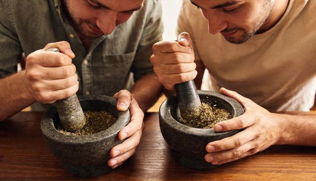 Grinding culinary herbs using granite mortars and pestles, two men collaborating in kitchen