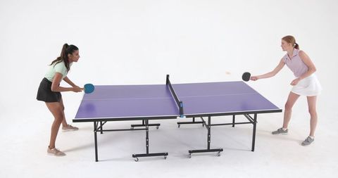 Energized women playing table tennis in white studio