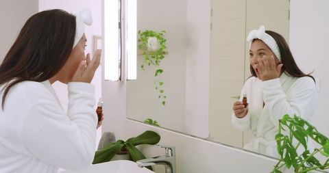 Woman applying face serum in modern bathroom for skincare routine