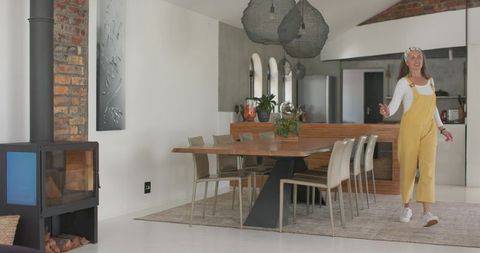 Woman wearing yellow overalls walking through bright modern open-plan kitchen dining area