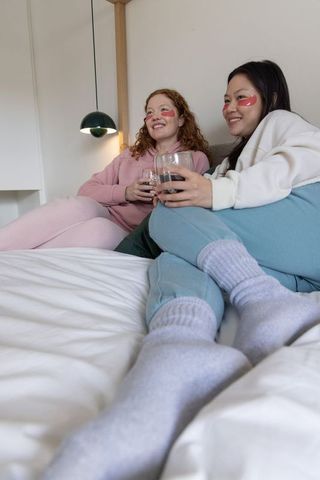 Multiethnic friends relaxing in loungewear with under-eye patches and stemless glasses