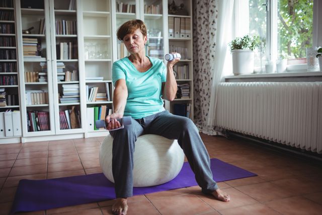 Senior woman exercising with dumbbells on exercise ball at home