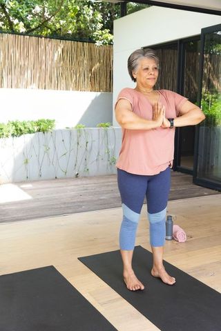 Senior woman practicing standing yoga and balance on covered patio deck with smartwatch