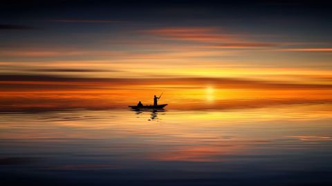 Silhouetted Fisherman in Canoe Against Vibrant Sunset Hues