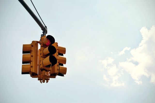 Brightly colored urban traffic light hanging on a pole against a clear sky. Can be used in articles or content discussing traffic management, city infrastructure, road safety, or urban planning.