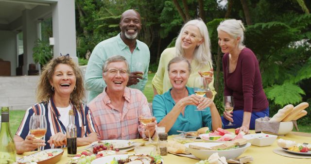 Image of diverse happy senior female and male friends eating lunch in garden. retirement lifestyle, spending quality time with friends.