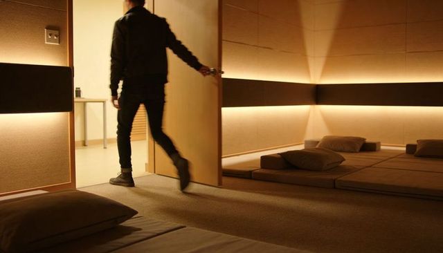 Man Entering Minimalist Lounge with Floor Cushions and Warm LED Backlighting