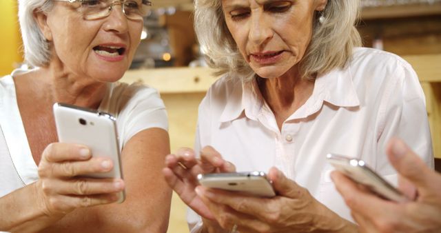 Senior women engaging in smartphone use and exploring technology together. Useful for themes related to senior citizens embracing digital technology, social media use among the elderly, and programs or services targeted toward teaching technology to older adults. Suitable for articles, promotional material, or educational resources focused on digital inclusion, tech-savvy seniors, and family tech support.