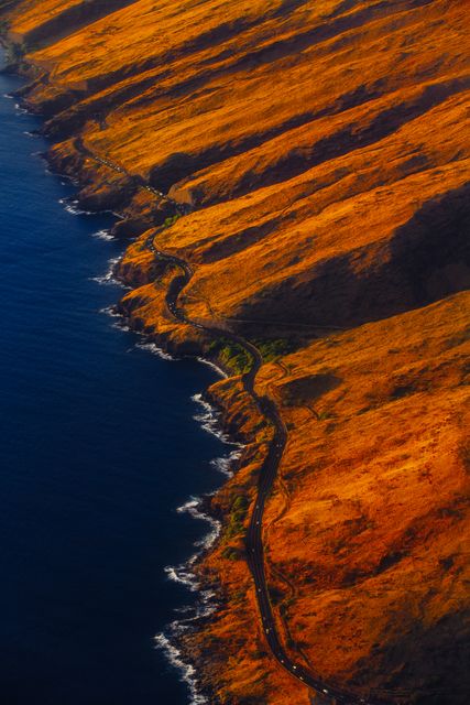 Image features a stunning aerial view of a winding coastal road beside rugged hills at sunset. The golden hue of the landscape contrasts beautifully with the deep blue ocean. Perfect for travel brochures, nature magazines, adventure blogs, or scenic wallpapers.