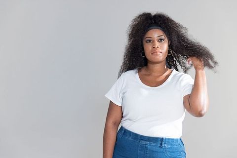 Confident african american woman standing with curly hair, wearing white tee and denim