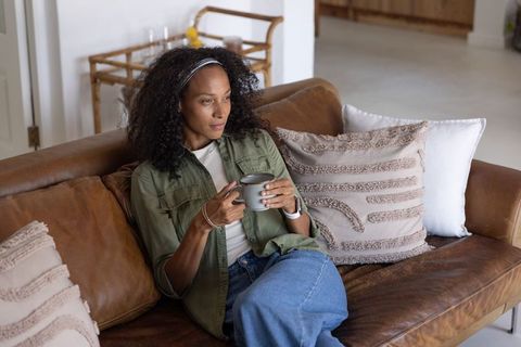 African american woman relaxing on leather couch holding mug among textured pillows
