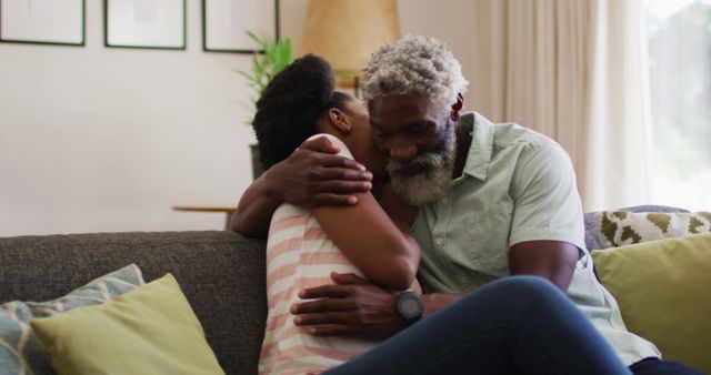 African American father and daughter sharing a heartfelt hug on a cozy couch. The image shows strong family bonds, affection, and the warmth of home. Suitable for use in advertisements, family-related articles, or content focusing on parenting, relationships, and love.