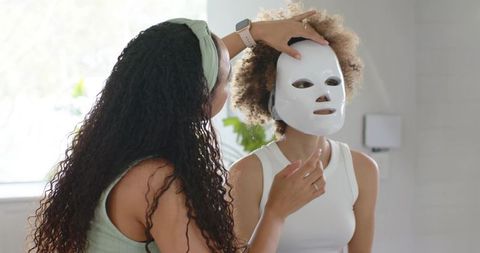 Applying led light therapy mask on african american woman in minimalist skincare studio