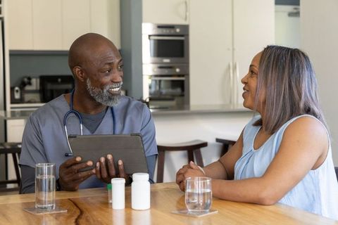 African american doctor consulting female patient at home using tablet and discussing medication