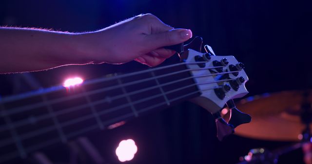 Hand tuning electric bass guitar on stage under purple lighting - Download Free Stock Images Pikwizard.com
