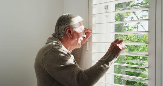 Senior man looking through white blinds near window bright daylight - Download Free Stock Images Pikwizard.com