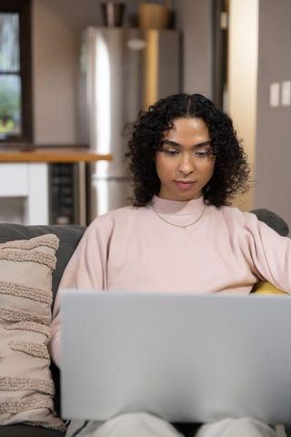 Non-binary adult working on laptop at home in cozy open-plan living room