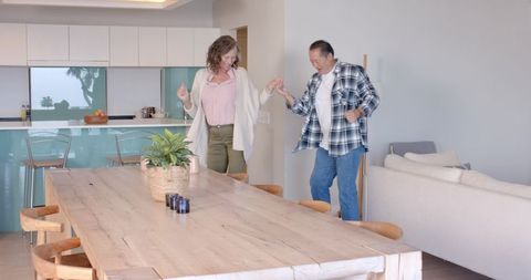 Happy Senior Couple Dancing Near Wooden Dining Table in Modern Kitchen
