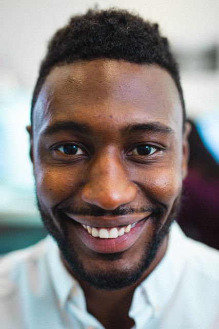 This image captures a close-up portrait of a smiling young African American businessman in a creative office environment. Ideal for use in business and corporate materials, diversity and inclusion campaigns, workplace culture promotions, and professional networking sites.