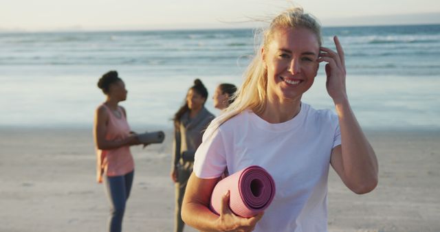 Smiling Woman Holding Yoga Mat on Beach with Friends - Download Free Stock Images Pikwizard.com