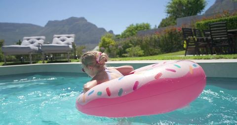Child reclining on pink donut float in turquoise backyard pool with mountain view and lounge chairs