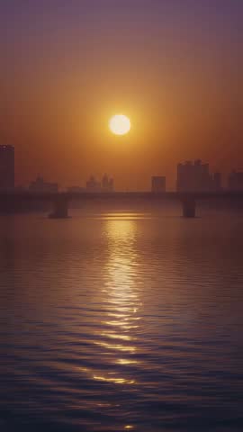 Vertical sunrise over river with bridge and city skyline reflecting golden light