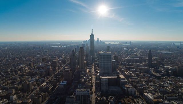 Sunlit downtown skyline with towering spire, aerial view of dense rooftops and harbor