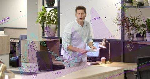 Male business analyst reviewing charts and reaching for papers while glancing left in modern office