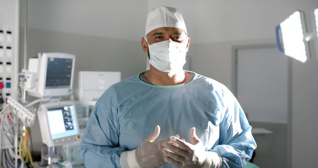 Portrait of biracial male surgeon with face mask and medical gloves in operating room. Medicine, healthcare, surgery and hospital, unaltered.