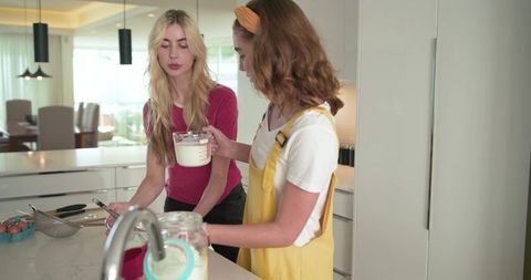 Young women measuring milk and prepping batter at bright modern kitchen island