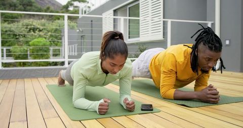 Diverse couple holding forearm plank on balcony deck, outdoor fitness partners training